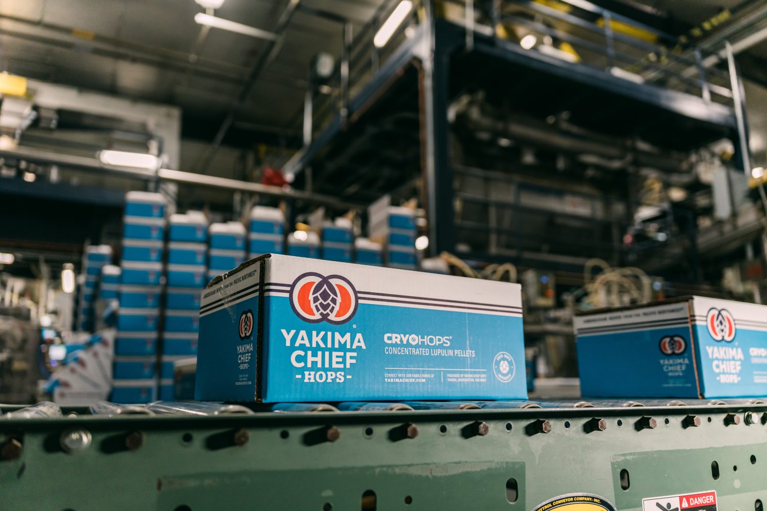 Yakima Chief Hops branded carton moving on a conveyor belt inside a manufacturing facility